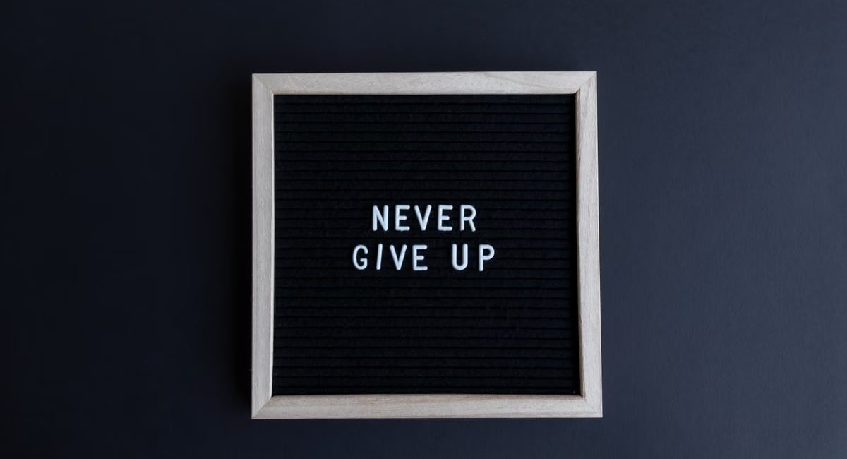 Inspirational letter board with 'Never Give Up' phrase on gray background.