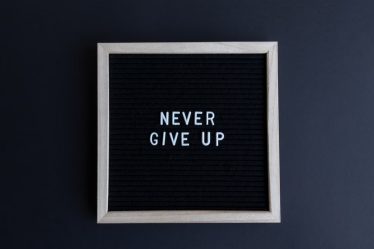 Inspirational letter board with 'Never Give Up' phrase on gray background.