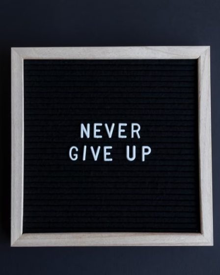 Inspirational letter board with 'Never Give Up' phrase on gray background.