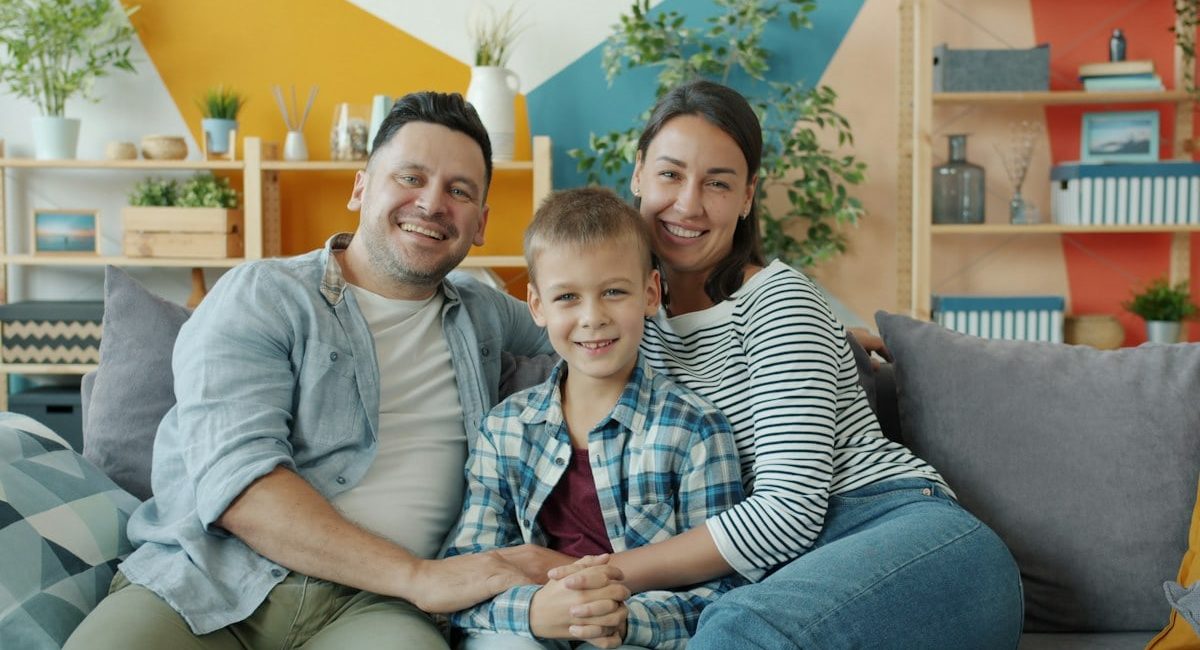 Portrait of cheerful young people woman, man and child smiling laughing sitting on couch in apartment and looking at camera. Family and emotions concept.