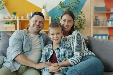 Portrait of cheerful young people woman, man and child smiling laughing sitting on couch in apartment and looking at camera. Family and emotions concept.