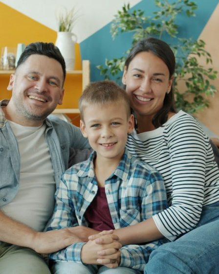Portrait of cheerful young people woman, man and child smiling laughing sitting on couch in apartment and looking at camera. Family and emotions concept.