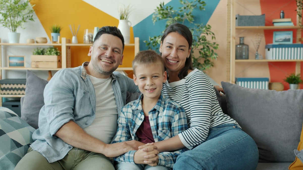 Portrait of cheerful young people woman, man and child smiling laughing sitting on couch in apartment and looking at camera. Family and emotions concept.